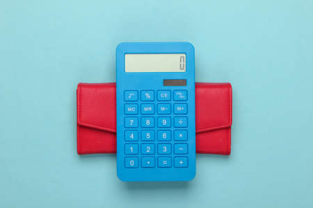 Manage family budget. Shopping costs. Blue calculator with red leather wallet on blue background. Top viewの写真素材