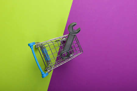 Supermarket shopping trolley with toy wrench on purple green background. Top viewの写真素材