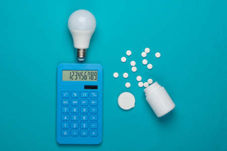 Creative calculation of the cost of medical expenses. Calculator and pills bottle, light bulb on blue background. I have an idea! Top view. Minimalismの写真素材