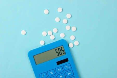 Calculation of the cost of medical expenses. Calculator and pills on blue background. SOS. Top view....