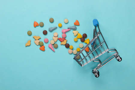 Veterinary tablets of vitamins with different shapes for cats and shopping trolley on blue...