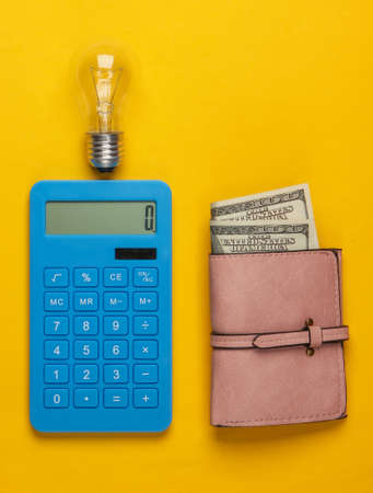 Calculation of costs for electricity. Wallet with money, calculator with light bulb on a yellow background. Top viewの写真素材