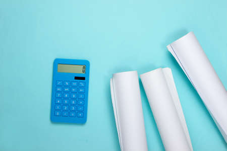Blueprint rolls and calculator on blue background. Calculation of the cost building a house. Top...