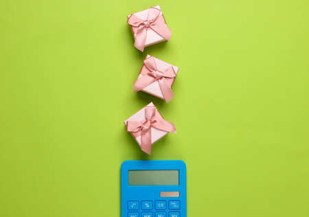 Calculator and gift boxes with bow on green background. Calculation of the value of the gift. Top...