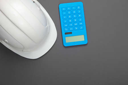 Engineering construction safety helmet and calculator on orange background. Calculation of the cost of repair or building house. Top view. Flat layの写真素材
