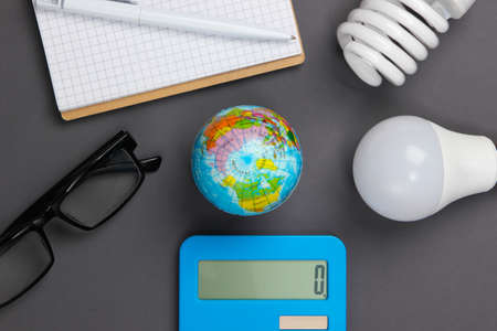 Energy saving analytics. Calculator with light bulbs, notebook, globe on gray background. Top viewの写真素材