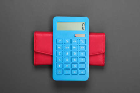Manage family budget. Shopping costs. Blue calculator with red leather wallet on gray background. Top viewの写真素材