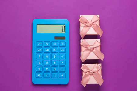 Calculator and gift boxes with a bow on purple background. Calculation of the value of the gift. Top view.の写真素材