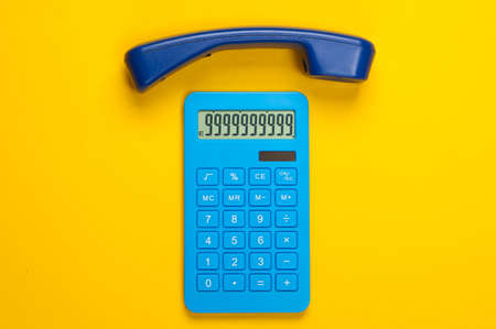 Calculator with handset office phone on yellow background. Top view