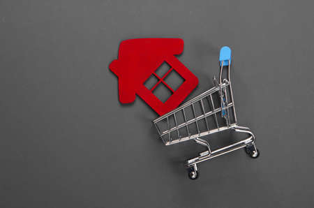 Buying a home concept. Shopping trolley with a house figure on gray background. Top view