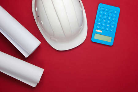 Engineering construction safety helmet, drawing rolls and calculator on red background. Calculation of the cost building a house. Top view. Flat layの写真素材