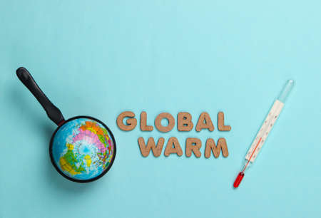 Global warming concept. Globe in pan and thermometer. Blue background. Top viewの写真素材