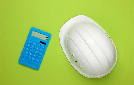 Engineering construction safety helmet and calculator on green background. Calculation of the cost of repair or building a house. Top view. Flat layの写真素材