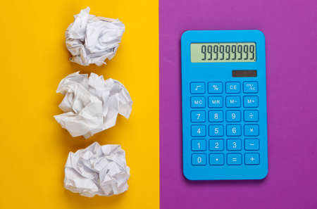 Blue calculator with crumpled balls of paper on purple yellow background. Top viewの写真素材