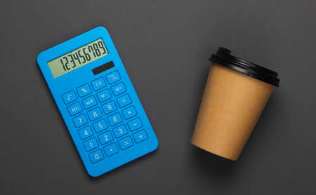 Calculator with a cardboard cup of coffee on gray background. Top viewの写真素材