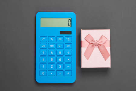 Calculator and gift box with bow on gray background. Calculation of the value of the gift. Top view.の写真素材