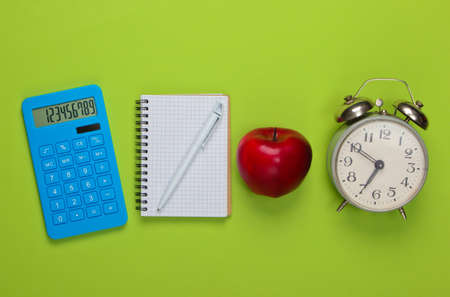 Calculator with notebook, apple, alarm clock on green background. Back to school. Education concept. Top viewの写真素材