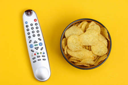 Movie time. Tv remotes and bowl with chips on a yellow background. Top viewの写真素材