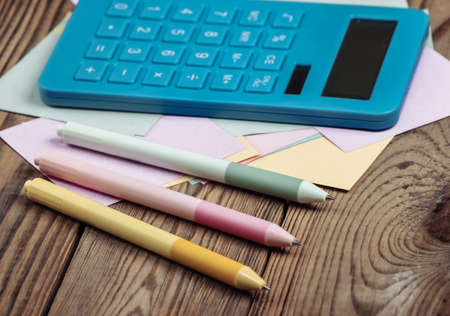 Calculator with memo papers and colored pens on a wooden table.の写真素材