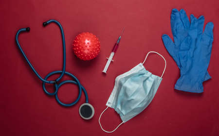 Coronavirus vaccine, diagnostics. Virus strain and syringe, stethoscope, mask, gloves on red background. Medical concept. Pandemicの写真素材