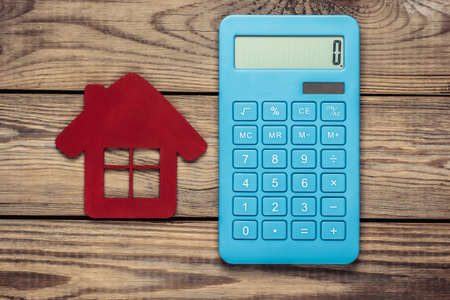 Calculation of the cost of renting or buying house. Calculator with red figure of house on wooden background. Top viewの写真素材
