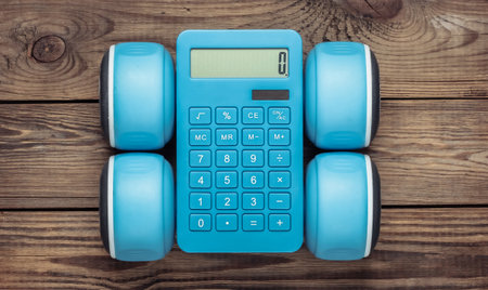 Blue calculator with dumbbells on a wooden table. Calorie counting