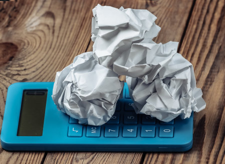 Blue calculator with crumpled paper balls on a wooden tableの写真素材