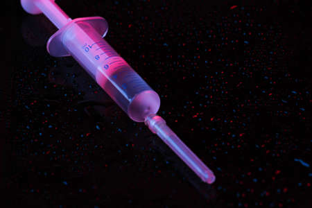 Syringe in neon red blue light on a black backgroundの写真素材