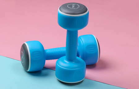 Plastic dumbbells on a blue pink pastel background.