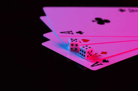 Playing cards of four aces with dice in neon blue-pink light on a black background. Game addiction. Pokerの写真素材