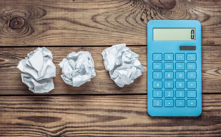 Blue calculator with crumpled paper balls on a wooden tableの写真素材