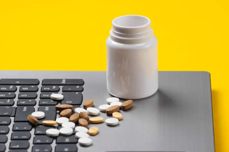Bottle of pills on laptop keyboard. Yellow studio background
