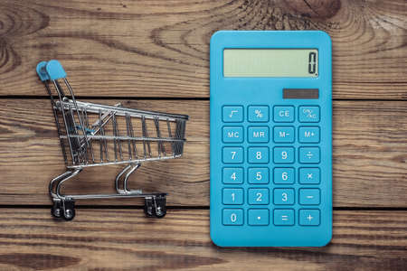 Calculation of the cost of shopping. Mini supermarket trolley, calculator on a wooden table. Top viewの写真素材