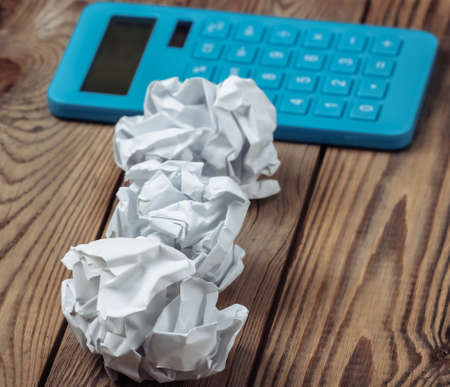 Blue calculator with crumpled paper balls on a wooden tableの写真素材