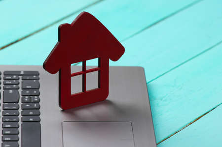 Laptop with house figure on a blue wooden background. Online rental reservation