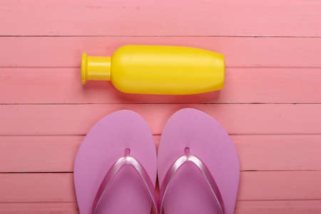 Beach vacation concept, summer background. Flip flops with bottle of sunblock on pink wooden...
