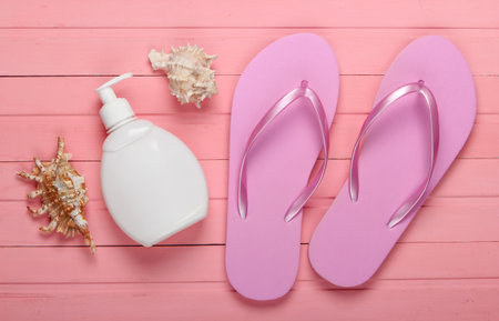 Beach vacation concept, summer background. Flip flops with bottle of sunblock, seashell on pink wooden background. Top viewの写真素材