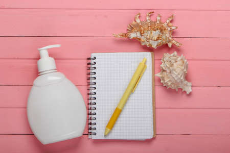 Memories of a beach holiday. Notebook with pen, sunblock, seashells on a pink wooden background. Top viewの写真素材