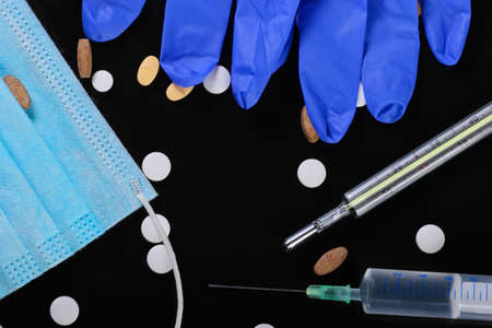 Medical still life. Syringe, thermometer, medical mask with gloves, pills. Black background....