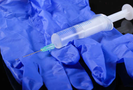 Close-up medical latex gloves with a syringe on a black background. Vaccination