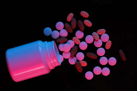 Bottle pills in gradient pink-blue neon light on black background.の写真素材