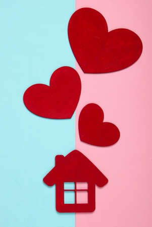 Red wooden hearts with a house figurine on pink blue pastel backgroundの写真素材