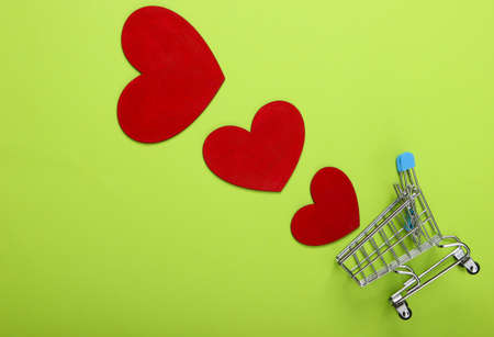 Mini supermarket trolley with red hearts on a green background. Shopping lover conceptの写真素材