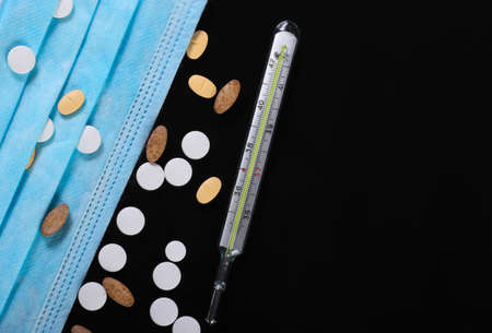 Medical still life. Thermometer, medical mask with pills. Black background.の写真素材