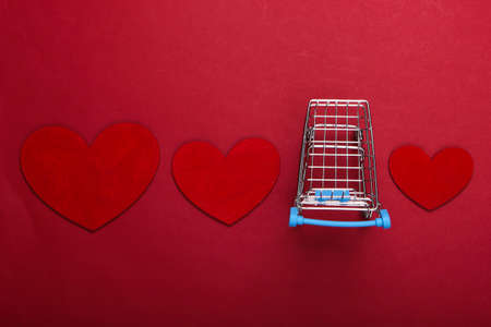 Mini supermarket trolley with red hearts on red background. Shopping lover conceptの写真素材