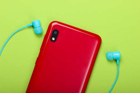 Smartphone with vacuum earphones on green  background. Top view