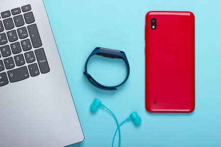 Modern gadgets. Laptop, smartphone and smart bracelet, vacuum earphones on blue background. Top viewの写真素材