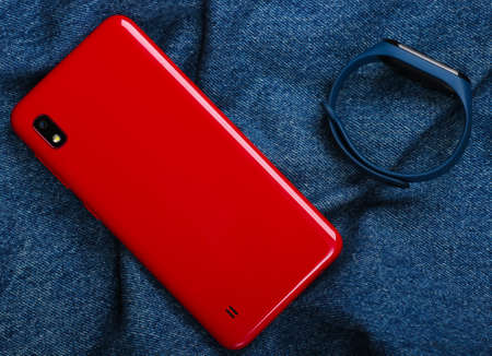 Red smartphone and smart bracelet on jeans background. Top viewの写真素材