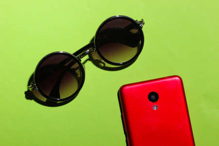 Fashionable glasses and smartphone on a green background. Women's accessoriesの写真素材