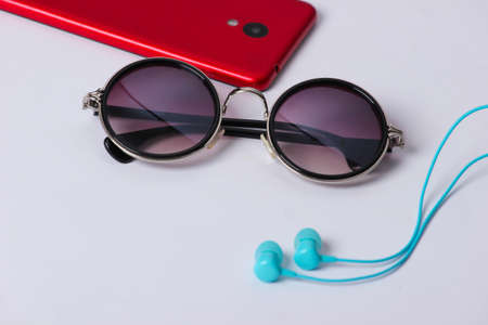 Women's accessories and gadgets on a yellow background. Earphones, stylish round sunglasses, smartphone on white backgroundの写真素材